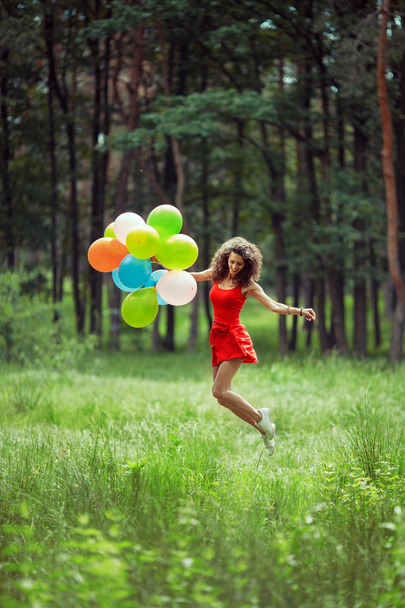 Beautiful young girl having fun at the summer park with colored balloons. Happy smile jump concept - Photo, Image