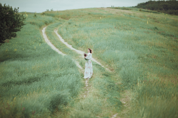 Young girl in vintage dress walking through sage flower field. - Foto, afbeelding