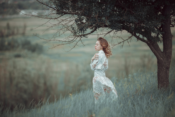 Mladá dívka v vintage šaty stojící poblíž osamělý strom - Fotografie, Obrázek
