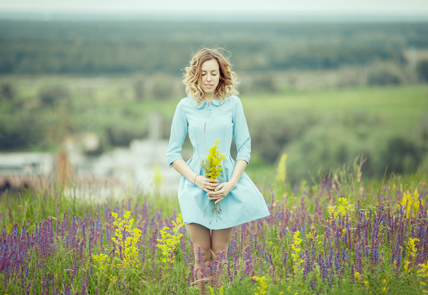 Young girl in vintage dress walking through sage flower field. - Foto, afbeelding