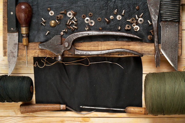 Herramientas artesanales de cuero sobre fondo de madera. Escritorio de artesanos. Pieza de cuero y herramientas hechas a mano. Vista superior
 - Foto, imagen
