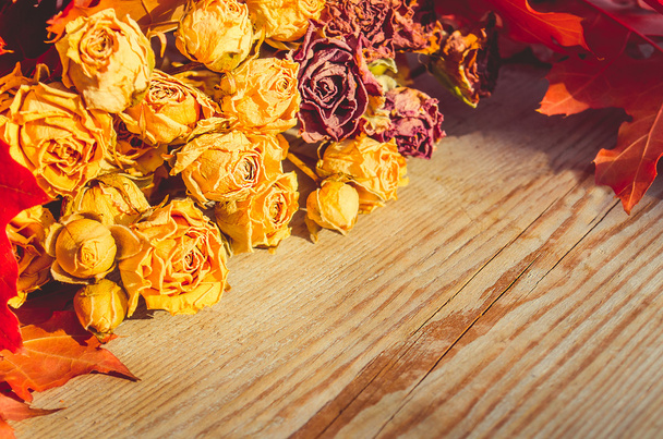 Kytice sušených růží a podzimní listí na dřevěné pozadí. - Fotografie, Obrázek