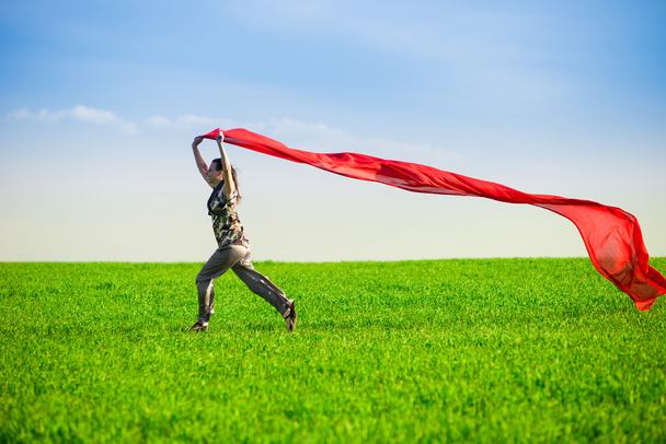 Beautiful young woman jumping on a green meadow with colored tissue - Photo, Image