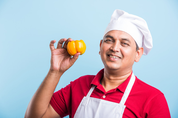 Indický šéfkuchař zobrazující Capsicum, asijského kuchaře a barevnou Capsicum, izolovaný na modrém pozadí - Fotografie, Obrázek
