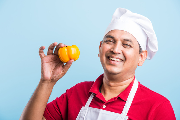indischen männlichen Koch zeigt Paprika, asiatischen männlichen Koch Koch und bunte Paprika, isoliert über blauem Hintergrund - Foto, Bild