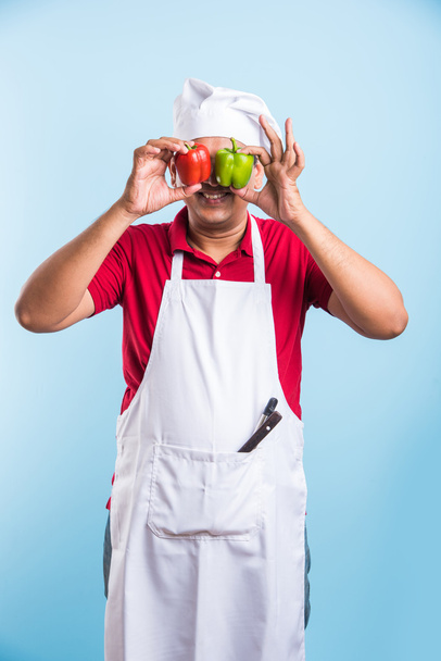 indian Male chef showing capsicum , asian male cook chef and colorful capsicum, isolated over blue background - Foto, Imagem