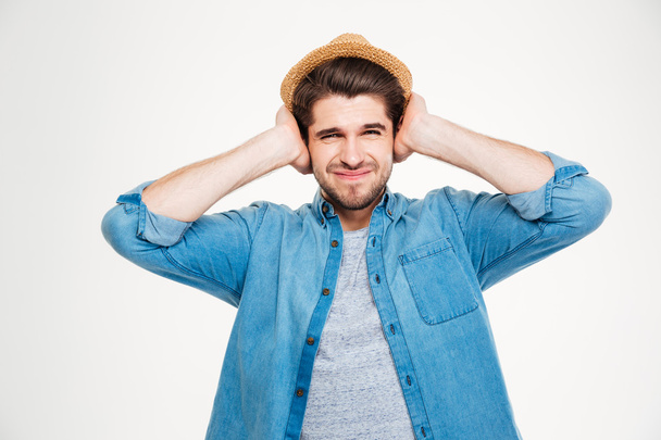 Frowning handsome young man covered ears by hands - Foto, Imagem
