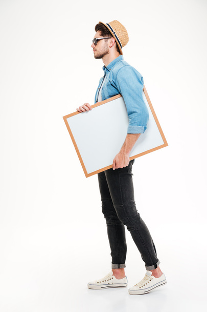 Full length of serious man walking and holding blank whiteboard - Φωτογραφία, εικόνα