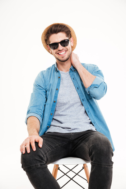 Happy young man in hat and sunglasses sitting on chair - Foto, Imagem
