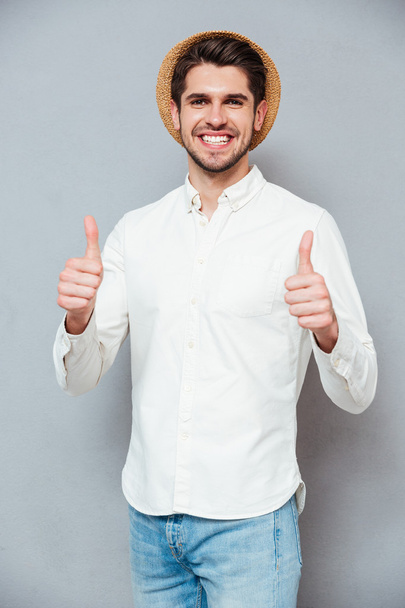 Hombre sonriente con sombrero mostrando los pulgares hacia arriba con ambas manos
 - Foto, Imagen