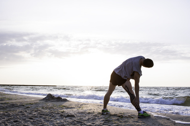 man with tattoo doing exercises on beach - Foto, Imagen