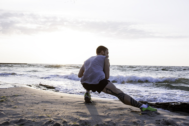 man with tattoo doing exercises on beach in morning - Foto, Bild