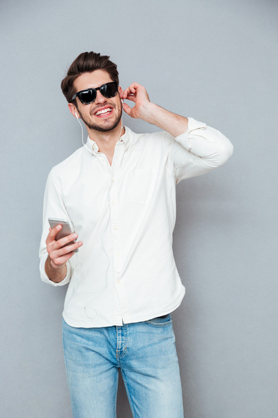 Smiling man in sunglasses listening to music from mobile phone - Фото, изображение