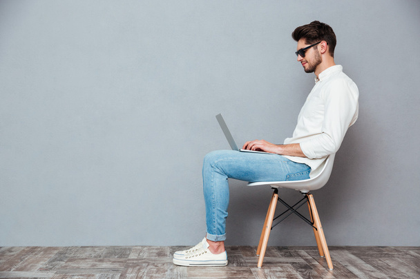 Serious man in sunglasses sitting on chair and using laptop - Photo, image