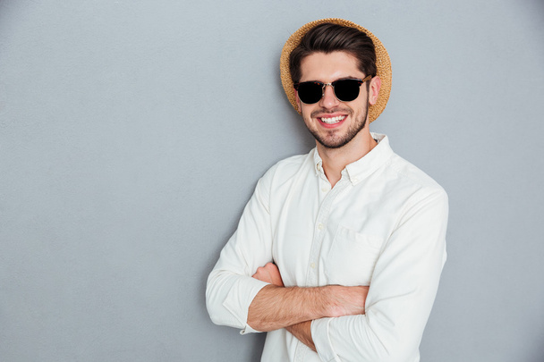 Веселый человек в шляпе и солнцезащитных очках, стоящий со сложенными руками
 - Фото, изображение