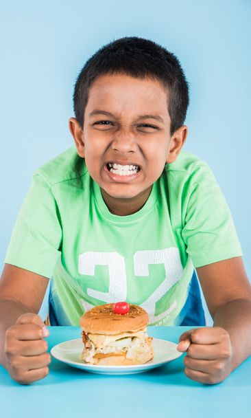 bonito indiana menino comer hambúrguer, pequeno asiático menino e hambúrguer, sobre azul fundo
 - Foto, Imagem