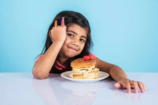 linda chica india comiendo hamburguesa, pequeña chica asiática y hamburguesa, aislado sobre fondo amarillo
 - Foto, Imagen