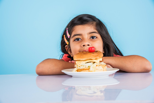 cute indian girl eating burger, small asian girl and burger, isolated over yellow background - Photo, Image
