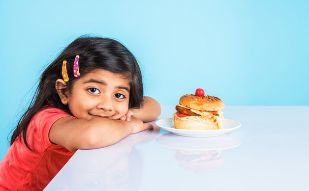 cute indian girl eating burger, small asian girl and burger, isolated over yellow background - Photo, Image