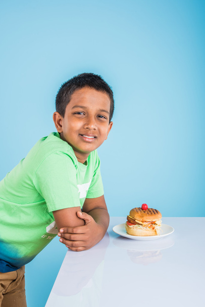 lindo indio chico y hamburguesa en pequeño plato blanco, pequeño asiático chico y hamburguesa, sobre colorido fondo
 - Foto, Imagen