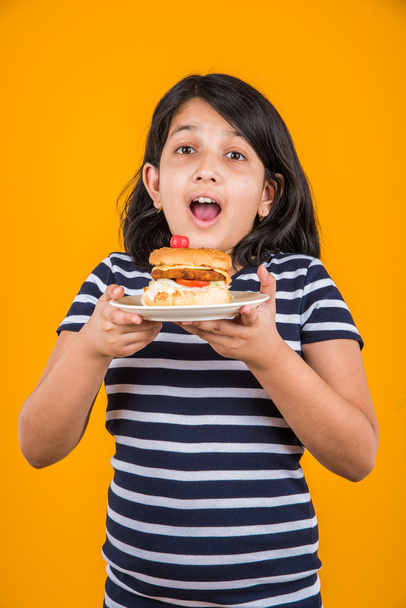 χαριτωμένο ινδική κορίτσι τρώει burger, μικρό ασιατικό κορίτσι και μπιφτέκι, απομονωμένη πολύχρωμο φόντο - Φωτογραφία, εικόνα