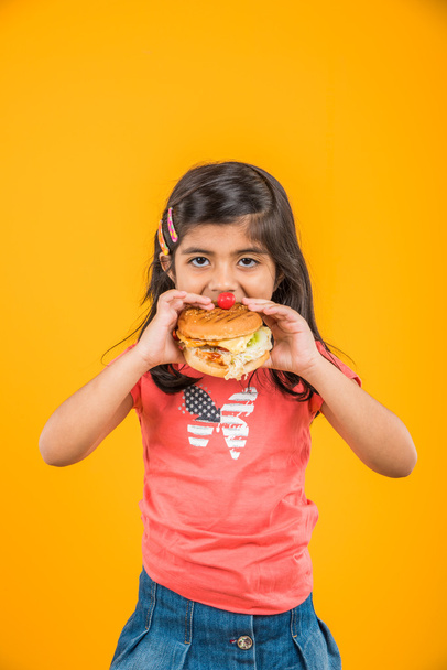 mignonne fille indienne manger hamburger, petite fille asiatique et hamburger, isolé sur fond jaune
 - Photo, image