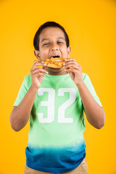 indio chico comer pizza sobre amarillo fondo
 - Foto, Imagen