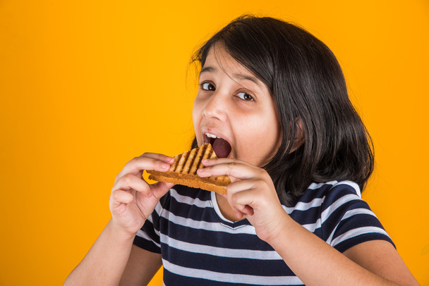 indiai lány, eszik, szendvicset, ázsiai lány és szendvics, szendvics, sárga háttér előtt pózol aranyos indiai lány - Fotó, kép