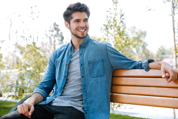 Handsome young man sitting on a bench smiling - Foto, Imagem