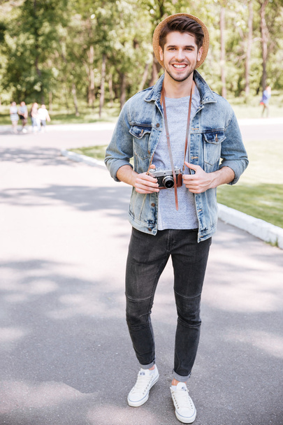 Handsome hipster guy holding camera wearing hat outdoors - 写真・画像