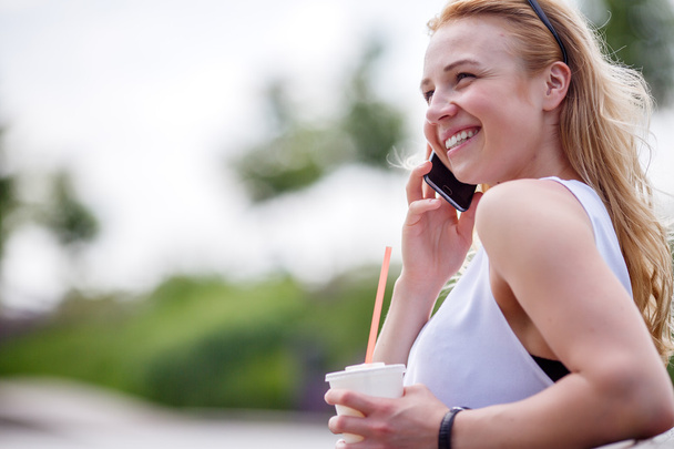 Young woman with milkshake and talking on mobile phone outdoors - Photo, image