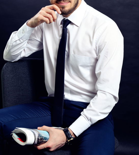 Успешный бизнесмен. Портрет уверенного молодого человека в формальной одежде, смотрящего в камеру и улыбающегося, держа руки скрещенными и стоя на сером фоне
 - Фото, изображение