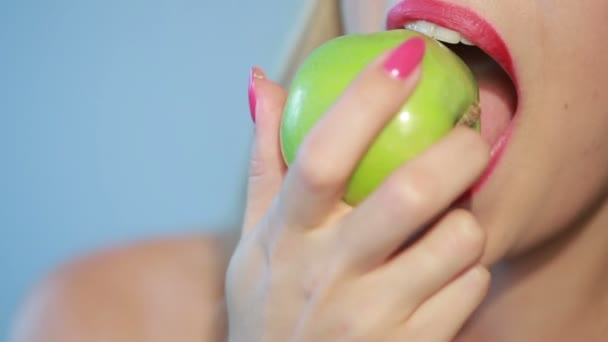beautiful girl eats a green apple on a blue - Video, Çekim