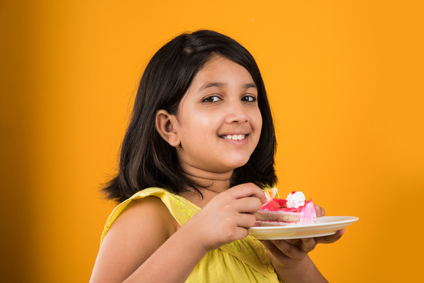 Indiai gyerek eszik torta vagy péksütemény, aranyos kislány enni tortát, étkezési eper torta, sárga háttér felett lány portréja - Fotó, kép