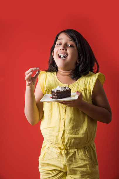 портрет индийского ребенка, поедающего торт или выпечку, милая маленькая девочка, поедающая торт, девушка, поедающая шоколадный торт или выпечку на цветном фоне
 - Фото, изображение