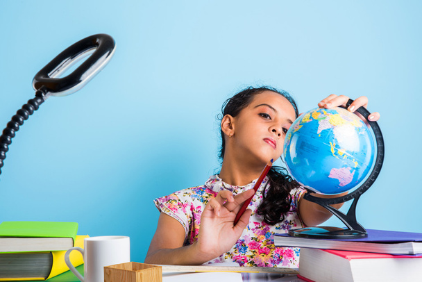 education and home concept - stressed student girl with books, indian girl child tired of studying or doing homework, asian girl studying and stressed, with globe toy and coffee mug - Foto, Bild