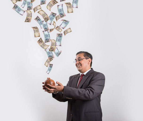 indian businessman catching flying currency in his piggy bank made up or clay, happy asian businessman with piggy bank under falling indian currency notes - Zdjęcie, obraz