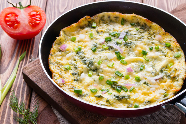 pan with a delicious omelette on a cutting board on a wooden background with vegetables - Foto, immagini