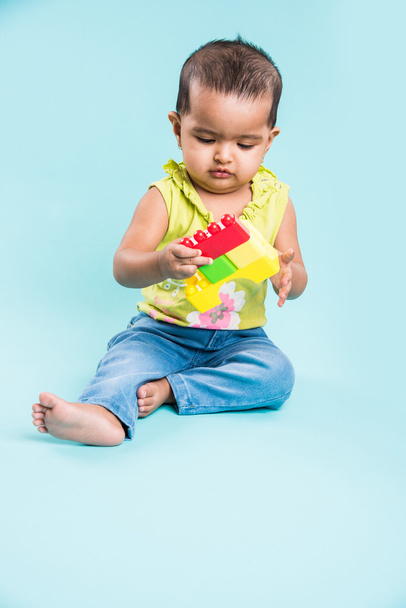 indiai kislány játszik a játékok vagy blokkok vagy lágy játékok több mint kék háttér, ázsiai csecsemő játszik a játékokkal, indiai kisgyermek játszott beltéri - Fotó, kép