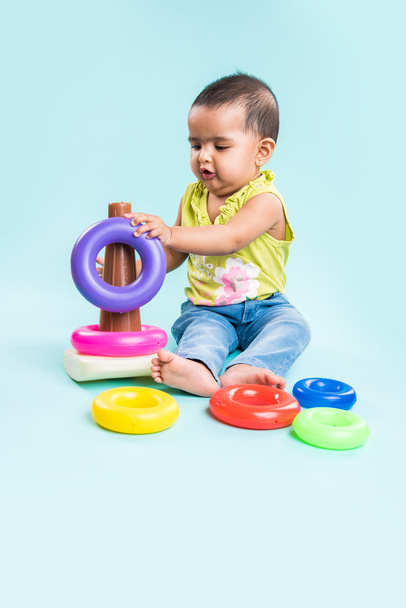 Bebé niña apilando anillos de colores, aislado sobre rojo, niña india jugando con el juguete, niña asiática jugando con el anillo
 - Foto, Imagen