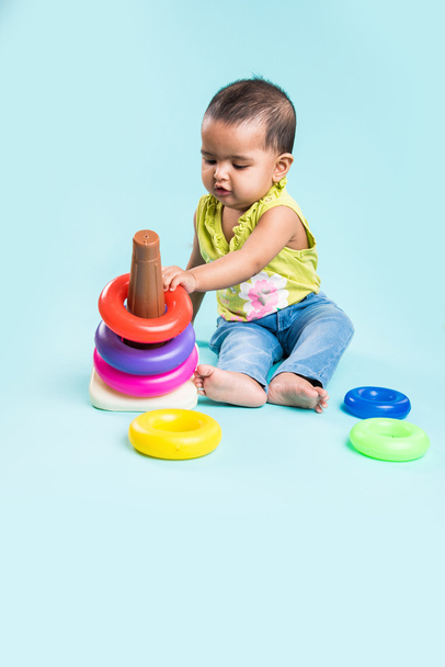 Baby meisje stapelen kleurrijke ringen, geïsoleerd via rood, Indiase klein meisje, spelen met speelgoed, Aziatische babymeisje spelen met ring - Foto, afbeelding