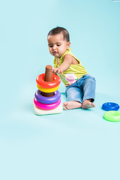 Bebé niña apilando anillos de colores, aislado sobre rojo, niña india jugando con el juguete, niña asiática jugando con el anillo
 - Foto, imagen
