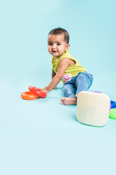 Baby meisje stapelen kleurrijke ringen, geïsoleerd via rood, Indiase klein meisje, spelen met speelgoed, Aziatische babymeisje spelen met ring - Foto, afbeelding