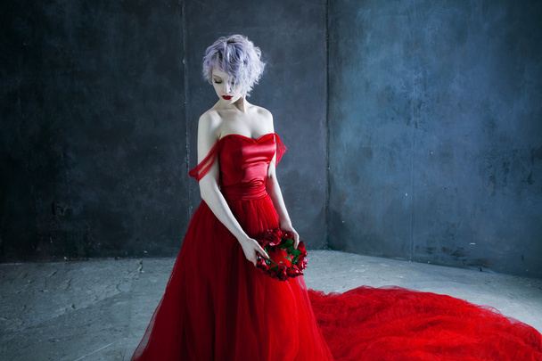 joven magnífica mujer en vestido rojo sostiene una corona de rosas. Fondo texturizado
 - Foto, Imagen