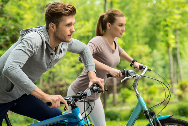 Cute man and woman riding bikes in park - Photo, image