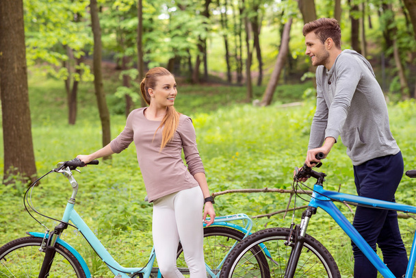 Joyful young man and woman walking with bikes - Φωτογραφία, εικόνα