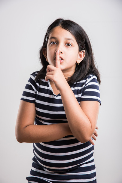 Kaunis intialainen pikkutyttö laittaa sormen huulille ja pyytää hiljaisuutta valkoisella taustalla. Aasialainen tyttö lapsi tekee Ole hiljaa ele kohti kameraa, intialainen pieni tyttö & hiljaisuus allekirjoita
 - Valokuva, kuva
