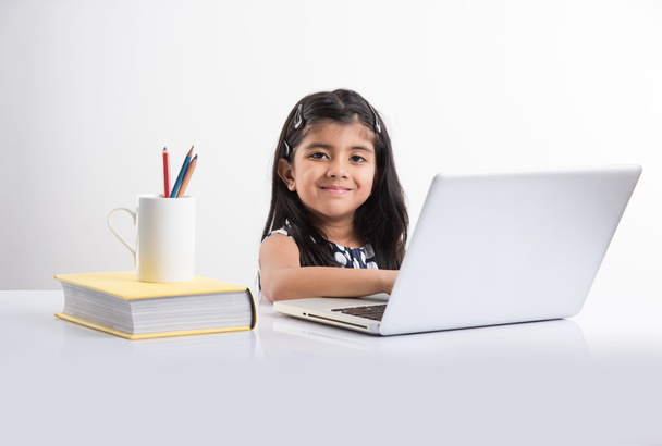 vrolijke Indiase meisje met behulp van laptop, Aziatische klein meisje spelen op laptop, geïsoleerd over witte achtergrond, schattige Indiase baby meisje spelen op laptop over studie tabel - Foto, afbeelding