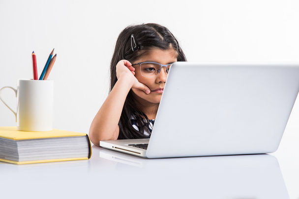 menina indiana alegre usando laptop, menina pequena asiática jogando no laptop, isolado sobre fundo branco, linda menina indiana jogando no laptop sobre a mesa de estudo
 - Foto, Imagem