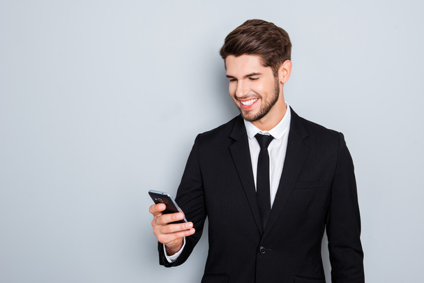 Cheerful young businessman in suit reading sms on smartphone - Foto, immagini